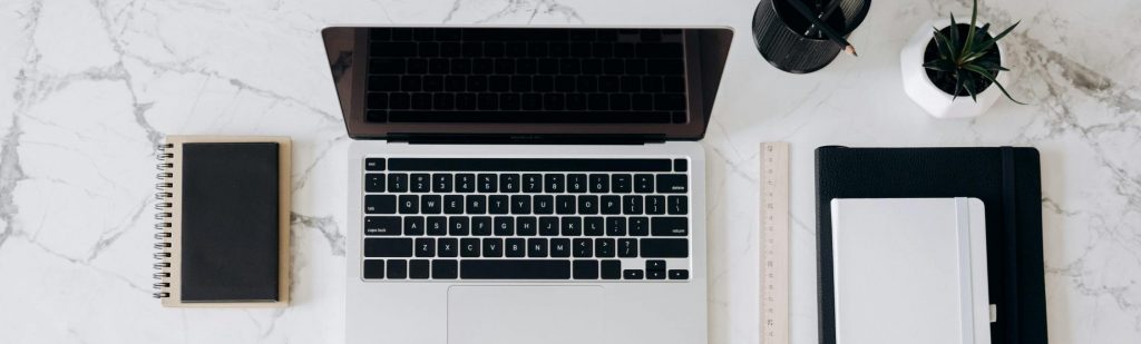 Top view of a stylish home office desk with a laptop, planner, and coffee cup, showing hands on a blueprint.